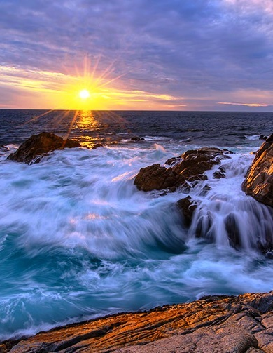 Preciosa puesta de sol azul satinado en el Océano Pacífico con olas bañando la costa rocosa.